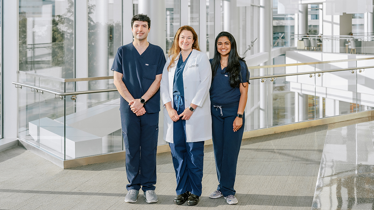 Three hospital employees posing in front of a large bay of windows.