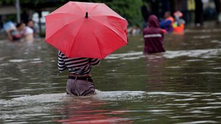 a man in waist deep flood water with a red umbrella