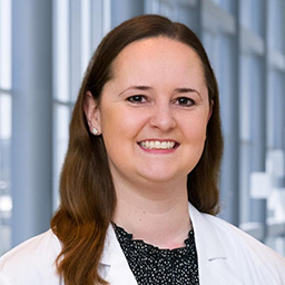 Dr. Jennifer Deacon wearing a dark ruffled shirt and a white lab coat standing in the Clements University Hospital lobby