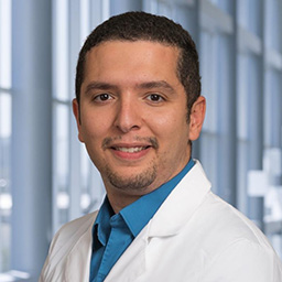 Dr. Mahmoud Elsayed wearing a bright blue shirt and a white lab coat standing in the Clements University Hospital lobby