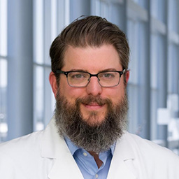 Dr. David Hoffman with a berd wearing a blue shirt and a white lab coat standing in the Clements University Hospital lobby