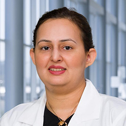 Dr. Sarah Khan wearing a dark shirt, and a white lab coat standing in the Clements University Hospital lobby