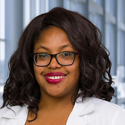 Dr. Henriette Mathis wearing glasses, and a white lab coat standing in the Clements University Hospital lobby