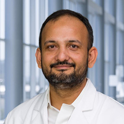 Dr. Usman Niaz wearing a white shirt, and a white lab coat standing in the Clements University Hospital lobby