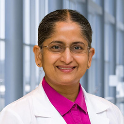 Dr. Jayasree Ramineni wearing glasses, a bright pink shirt, and a white lab coat standing in the Clements University Hospital lobby