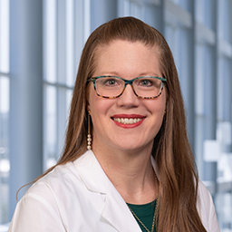 Dr. Jaxlyn Albin wearing a white lab coat and a green shirt standing in the Clements University Hospital lobby